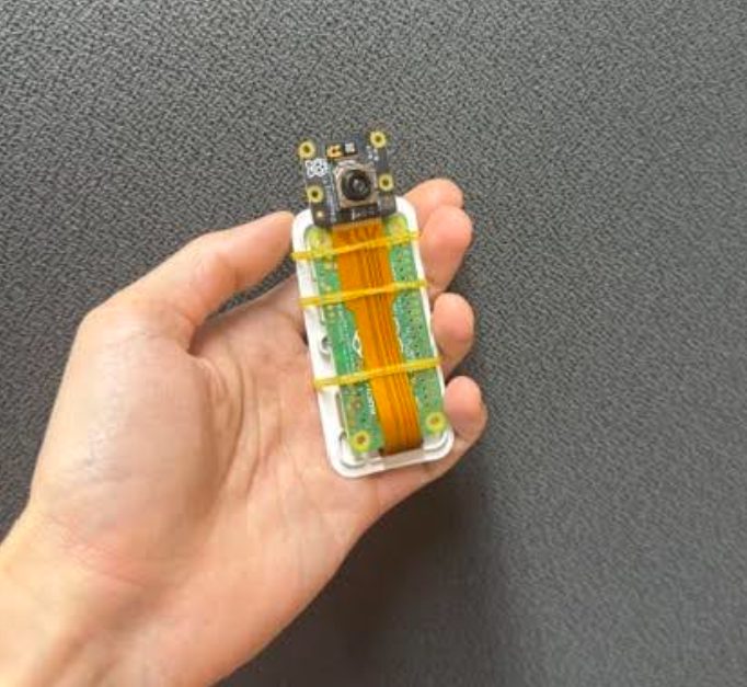 専用ケースに組み込まれた基板とカメラモジュール。オレンジ色のリボンケーブルが上部のカメラへ伸びている。